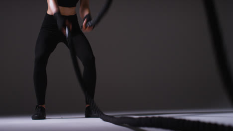 Close-Up-Studio-Shot-Of-Mature-Woman-Wearing-Gym-Fitness-Clothing-Doing-Cardio-Exercise-With-Battle-Ropes